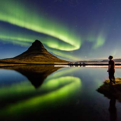 Man by water watching northern lights